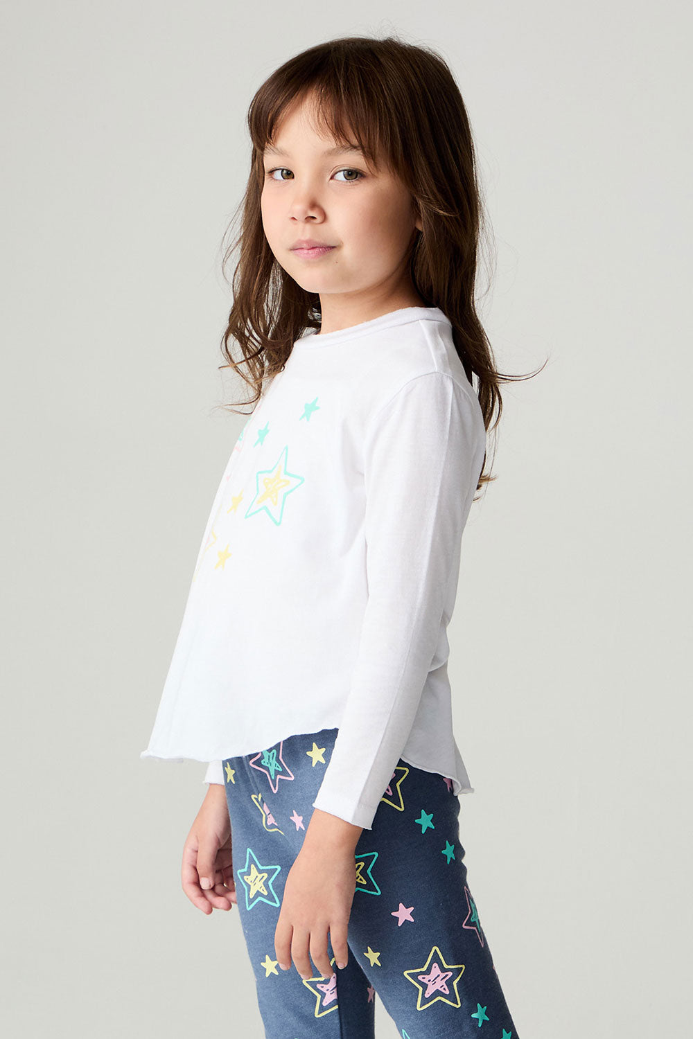 Side view of a girl wearing the Chaser Under The Stars Girls Tee on a neutral background with hands on legs
