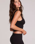 Side view of a woman wearing the Chaser Verze Black Top on a neutral background with black skirt