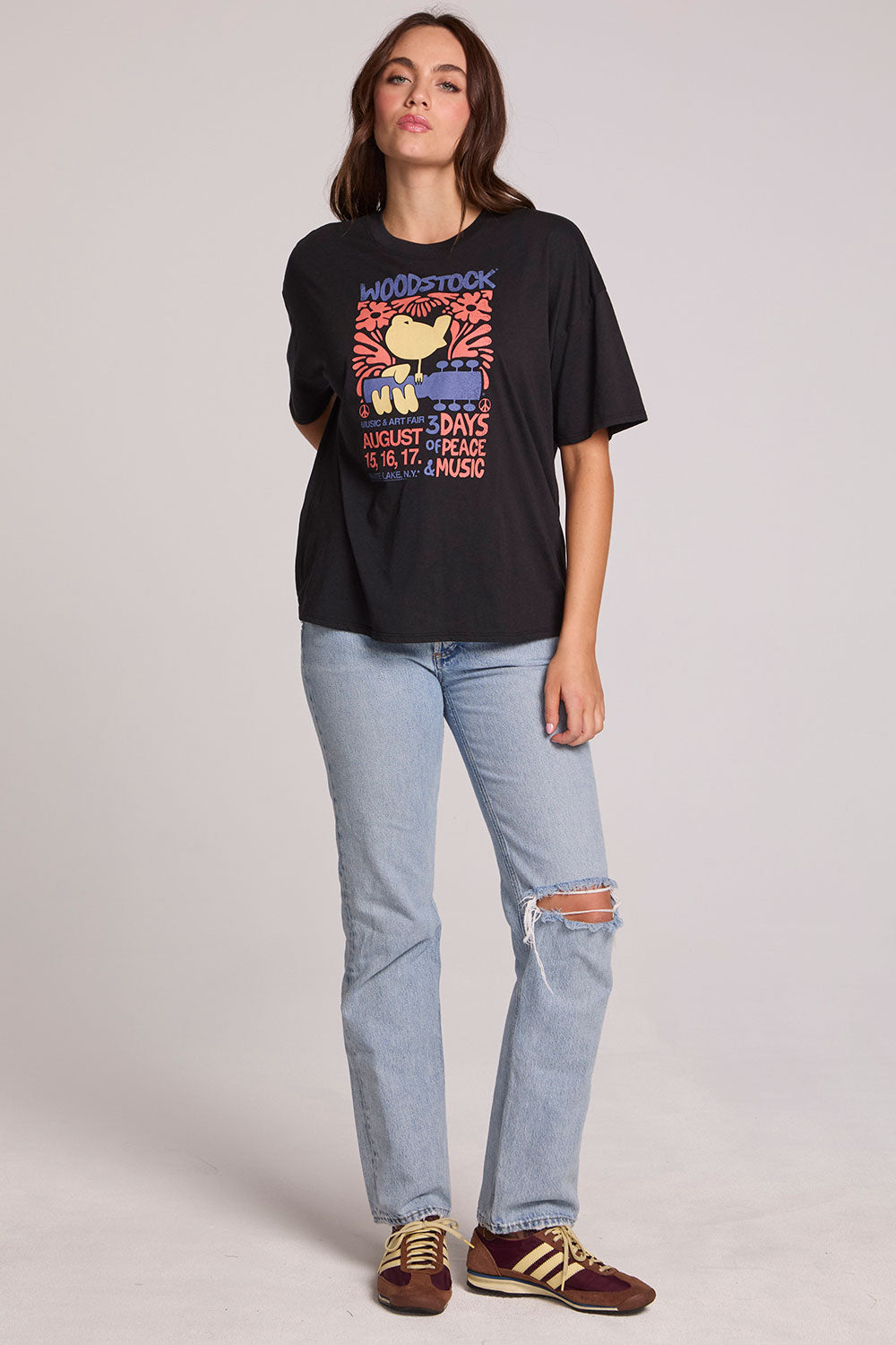 Full body front view of a woman wearing the Chaser  Woodstock Bird on Guitar Tee on a neutral background