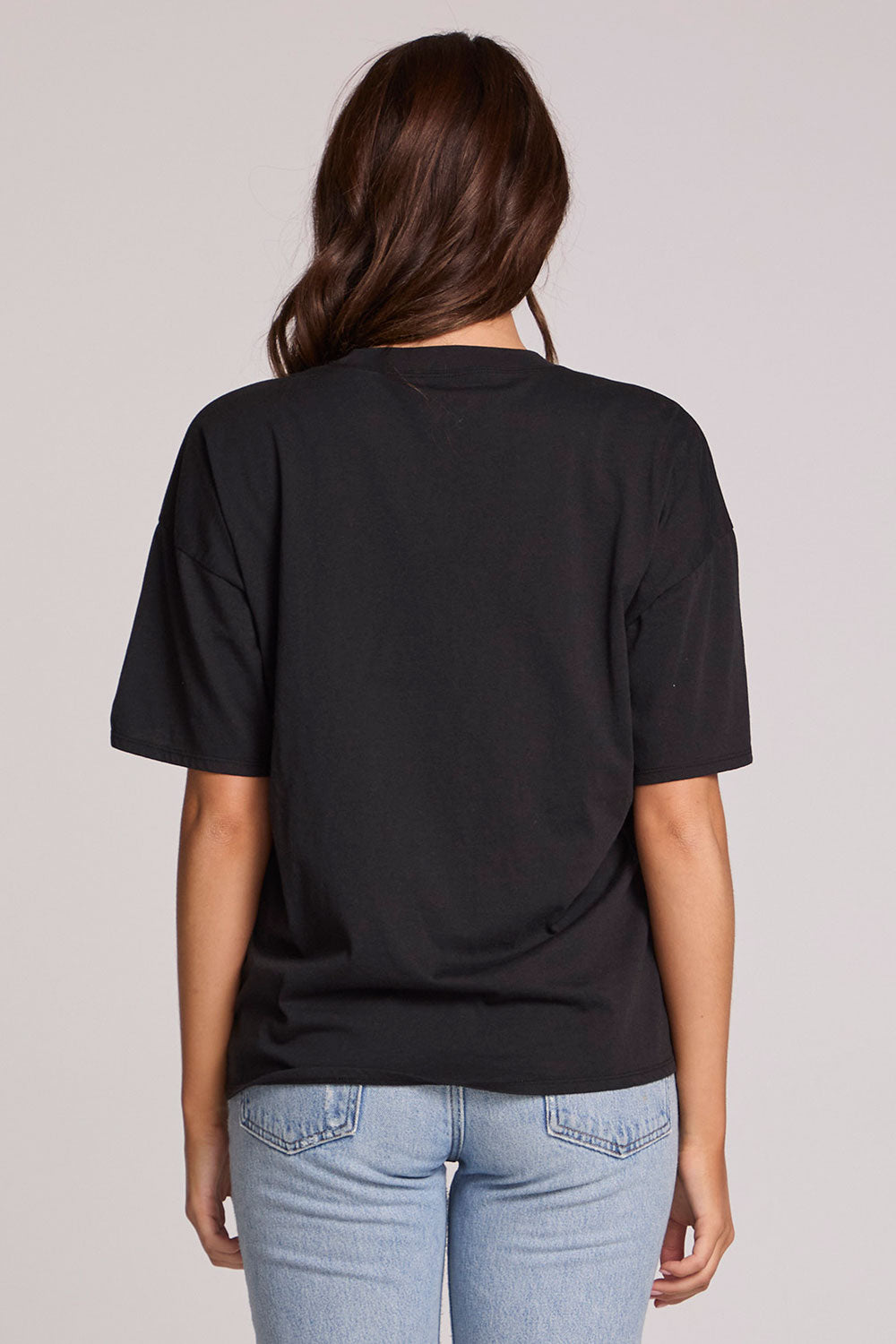 Back view of a woman wearing the Chaser  Woodstock Bird on Guitar Tee on a neutral background and jeans