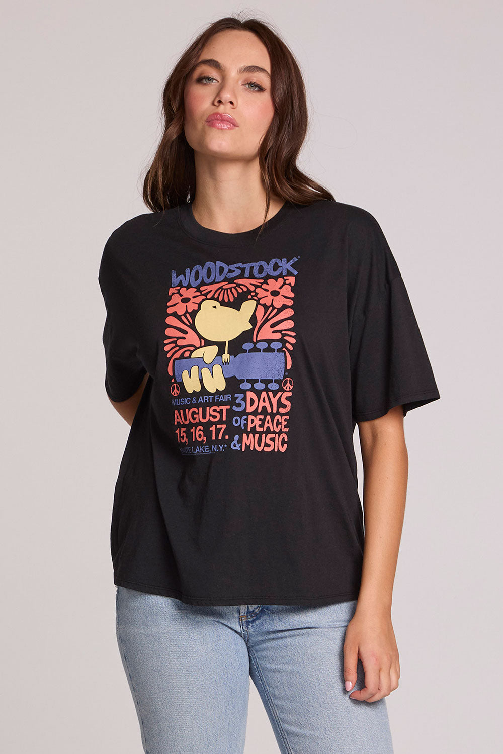 Front view of a woman wearing the Chaser  Woodstock Bird on Guitar Tee on a neutral background with bluejeans