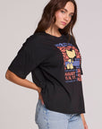 Side view of a woman wearing the Chaser  Woodstock Bird on Guitar Tee on a neutral background with hand on hip