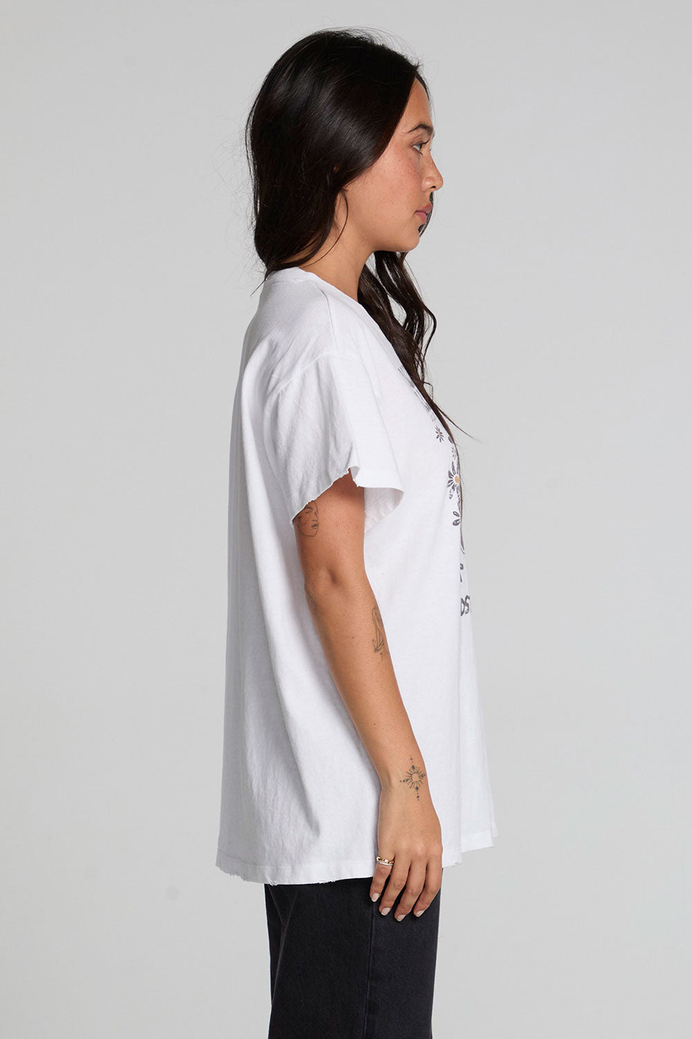 Side view of a woman wearing the Chaser Woodstock Music And Art Fair Tee on a neutral background with black pants