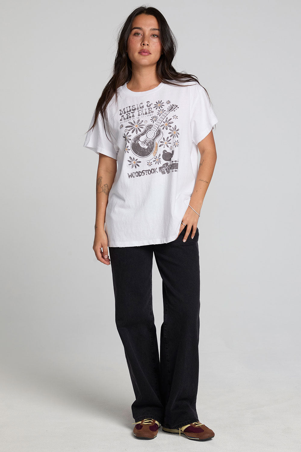 A full body front view of a woman wearing the Chaser Woodstock Music And Art Fair Tee on a neutral background