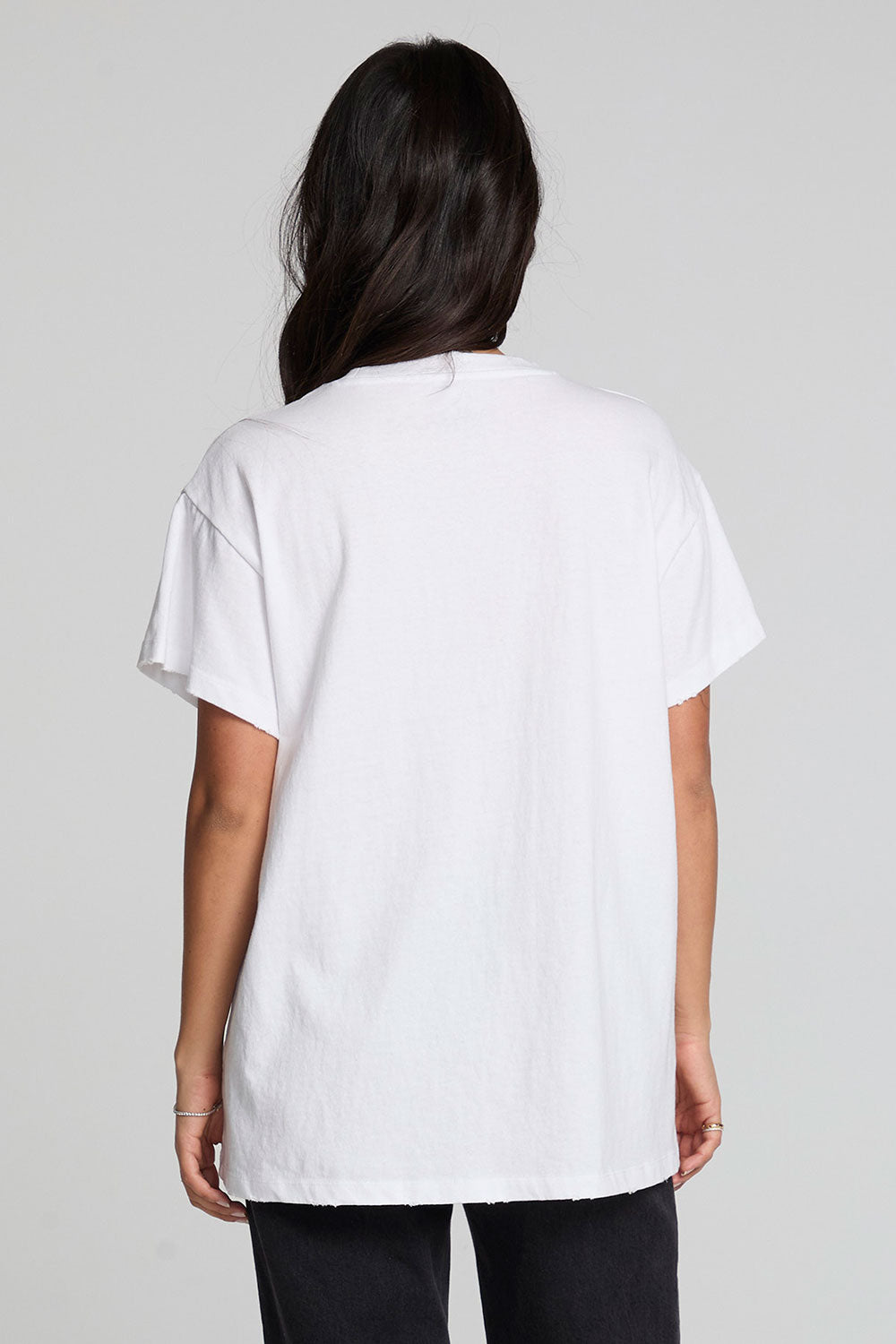 Back view of a woman wearing the Chaser Woodstock Music And Art Fair Tee on a neutral background with pants