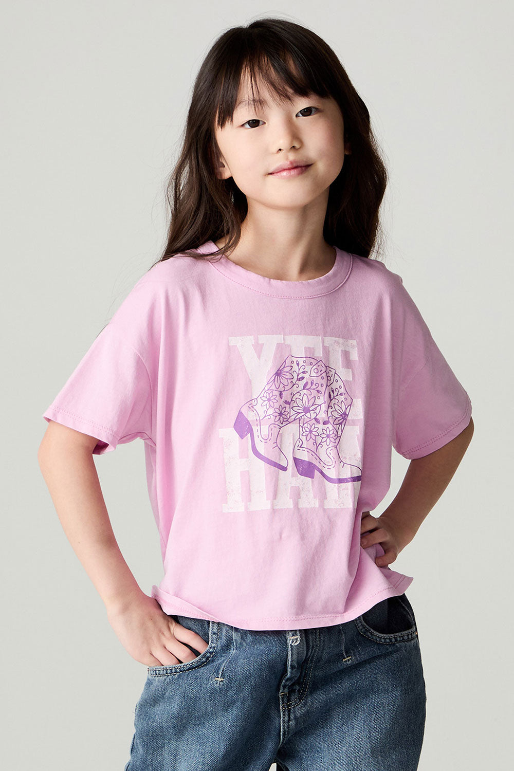Front view of a girl wearing the Chaser Yee Haw Girls Tee and jeans on a neutral background with hands on hips