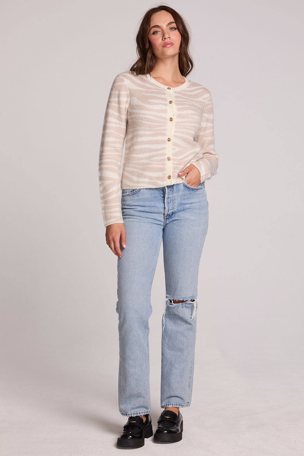 Full body front view of a woman wearing the Chaser  Zebra Dream Striped Cardigan and jeans on a neutral background with one hand in pocket