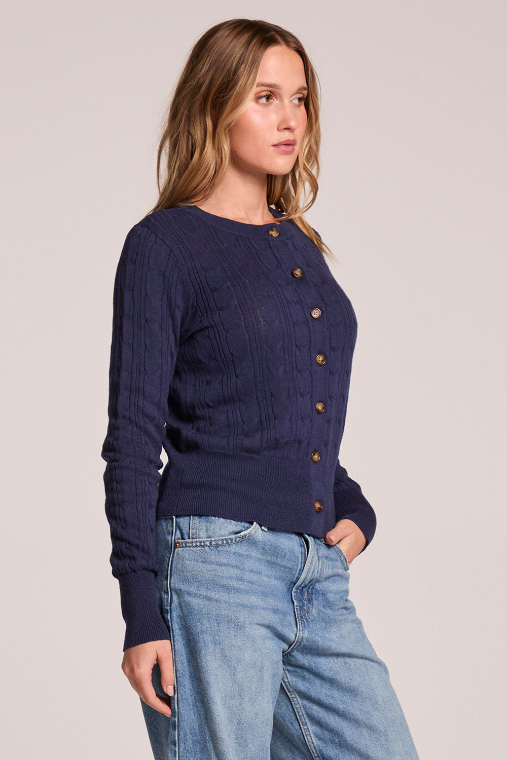 Siide view of a woman wearing the Chaser  Eliza Admiral Cardigan on a neutral background with one hand in her pocket