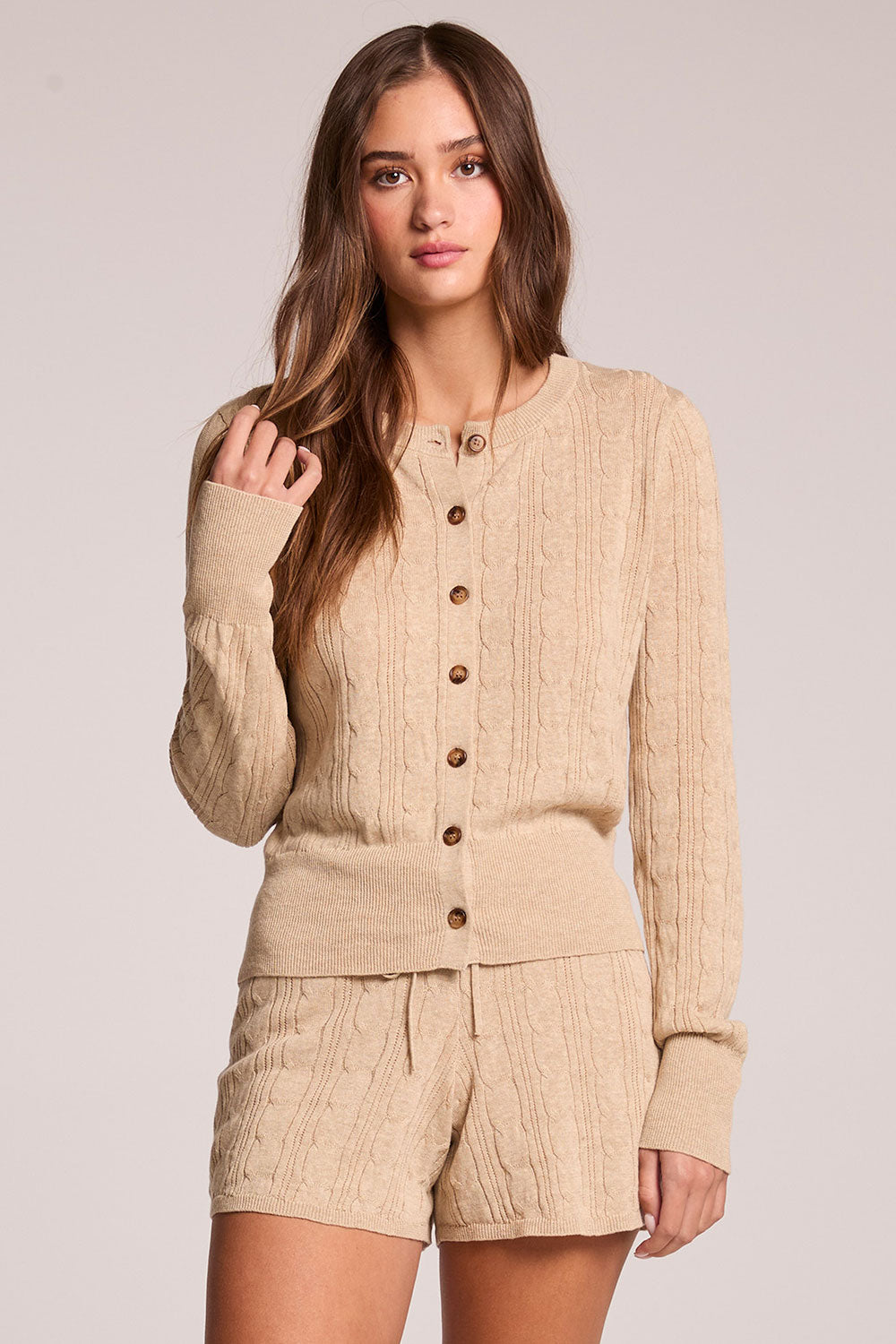 Front view of a woman wearing the Chaser Eliza Khaki Cardigan and shorts on a neutral background with one hand up