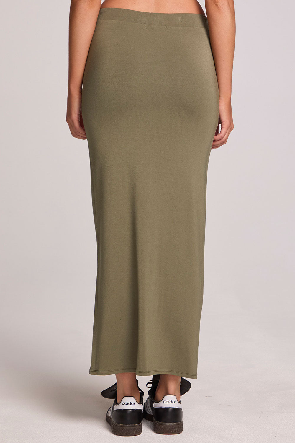 Back view of a woman wearing the Chaser Eloyse Forager Green Skirt on a neutral background with sneakers