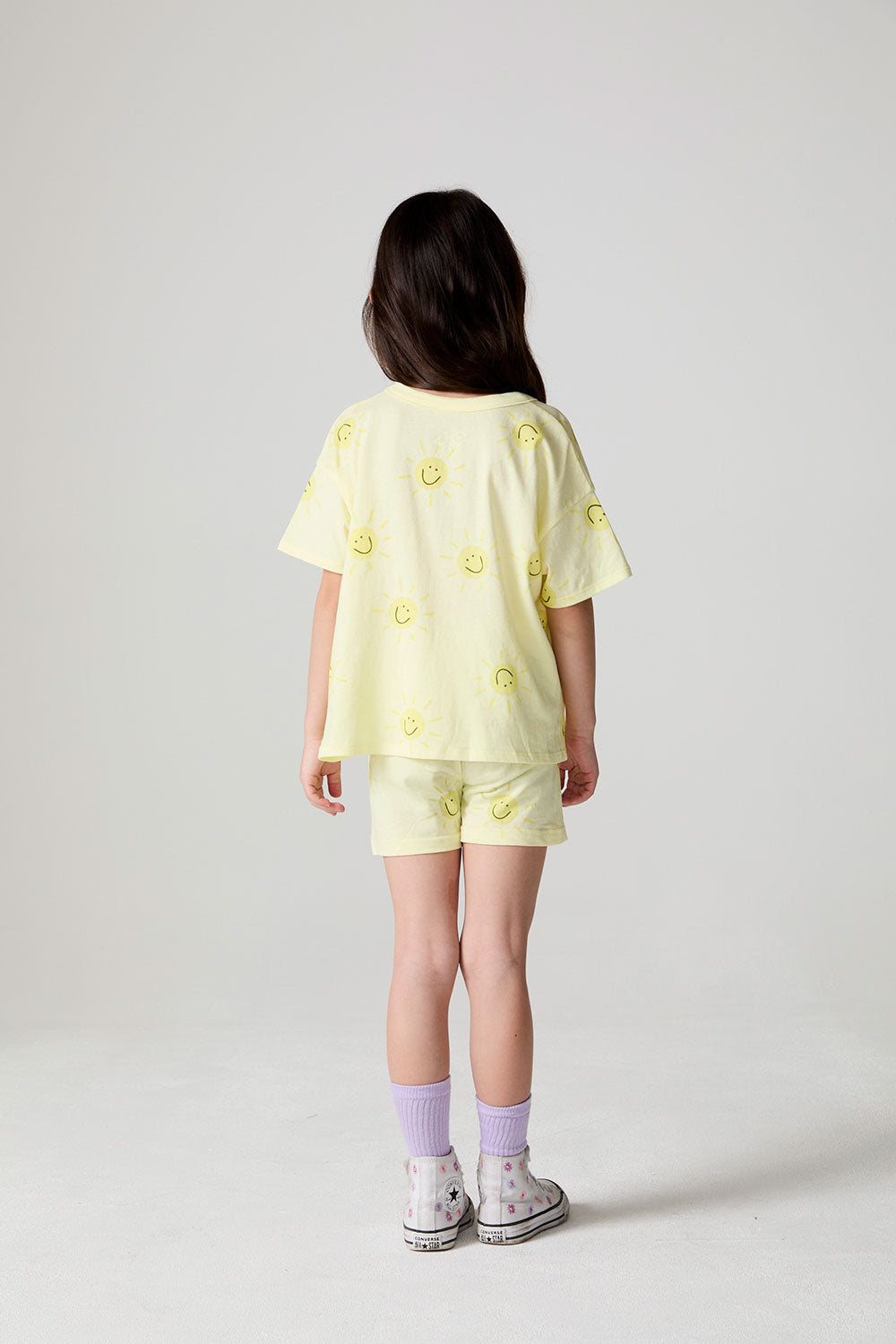 Back view of a girl wearing the Chaser Happy Happy Tee on a neutral background
