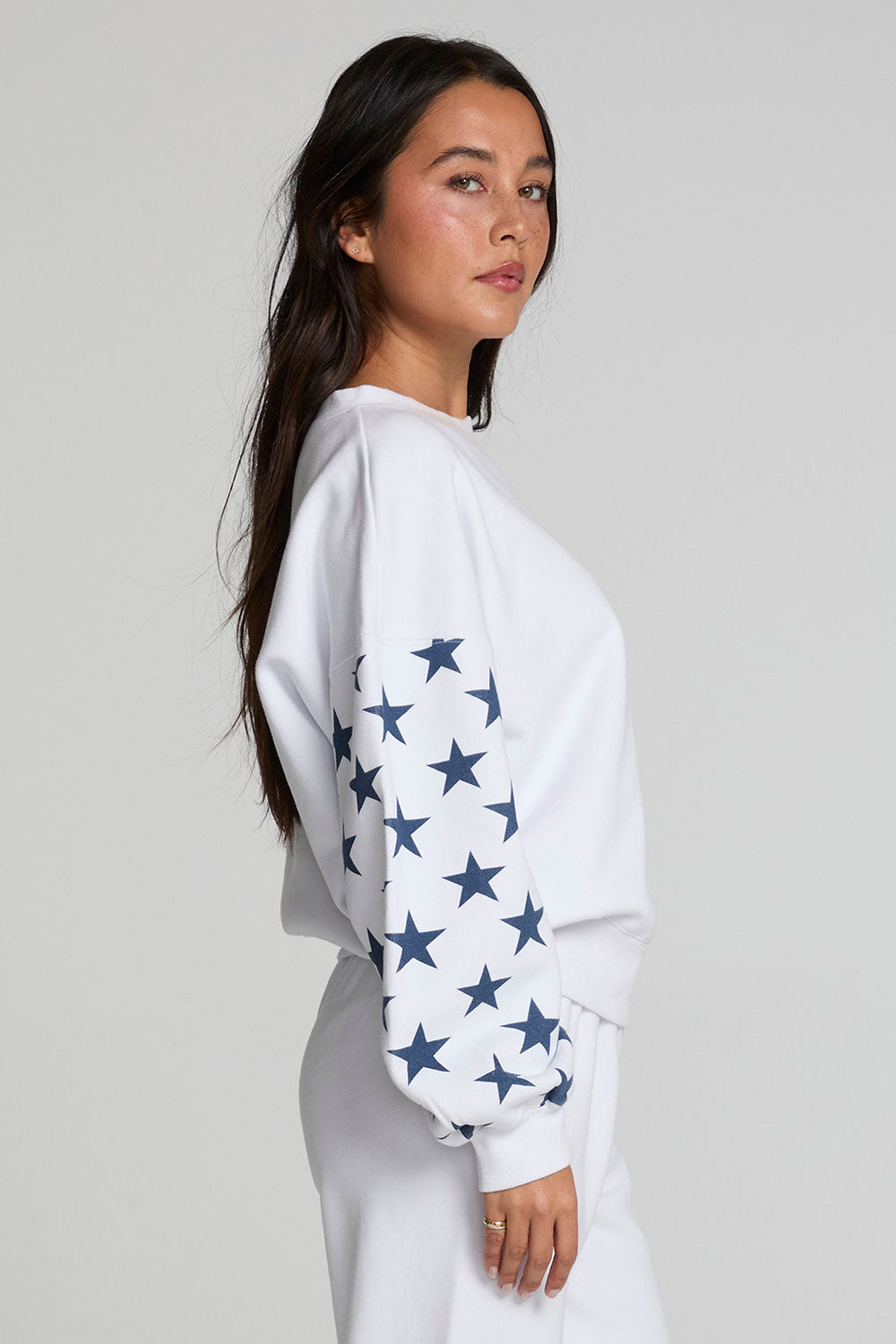 Side view of a woman wearing the Chaser   High Spirits Long Sleeve on a neutral background with pants