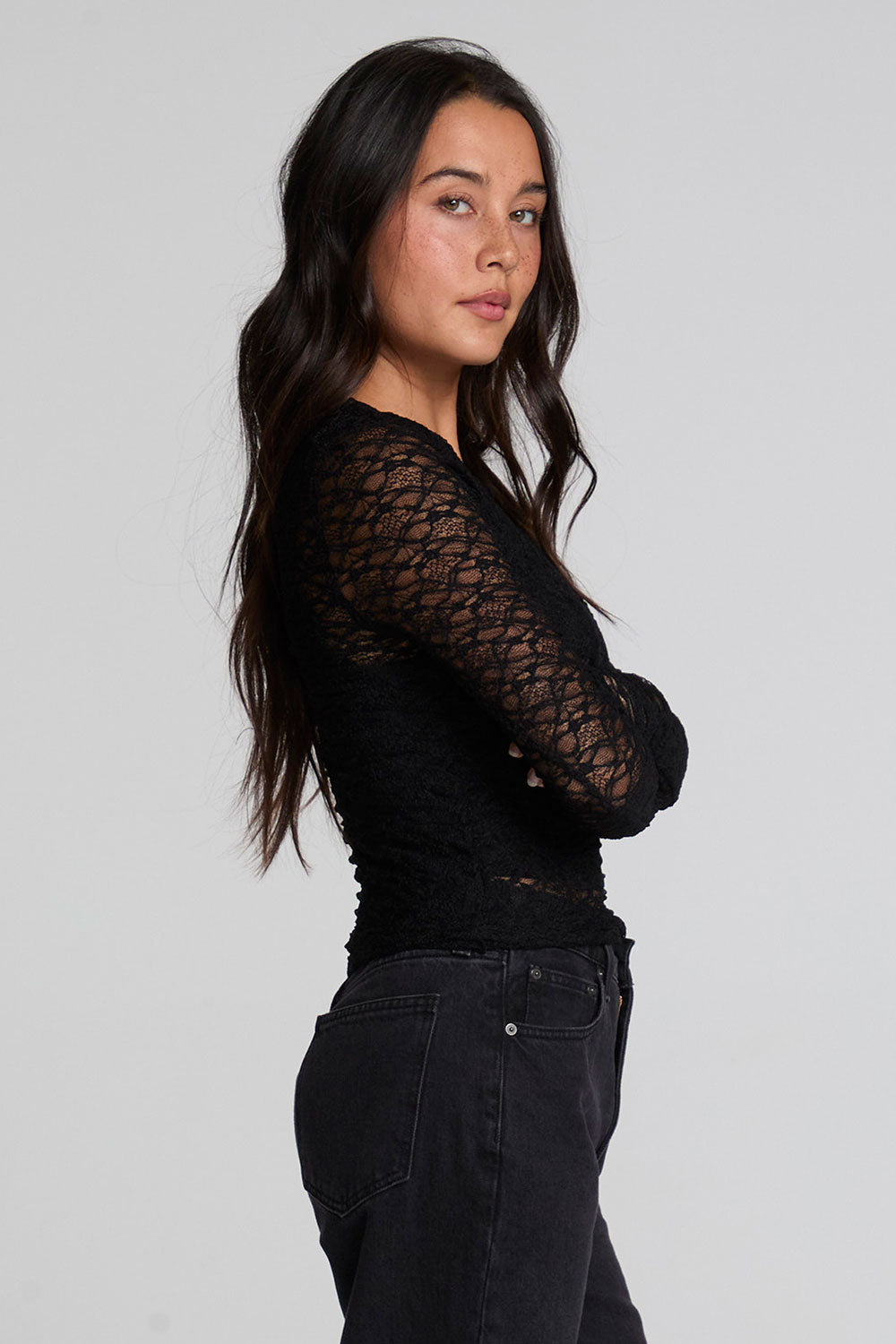 Side view of a woman wearing the Chaser Kevin Black Longsleeve on a neutral background with black pants