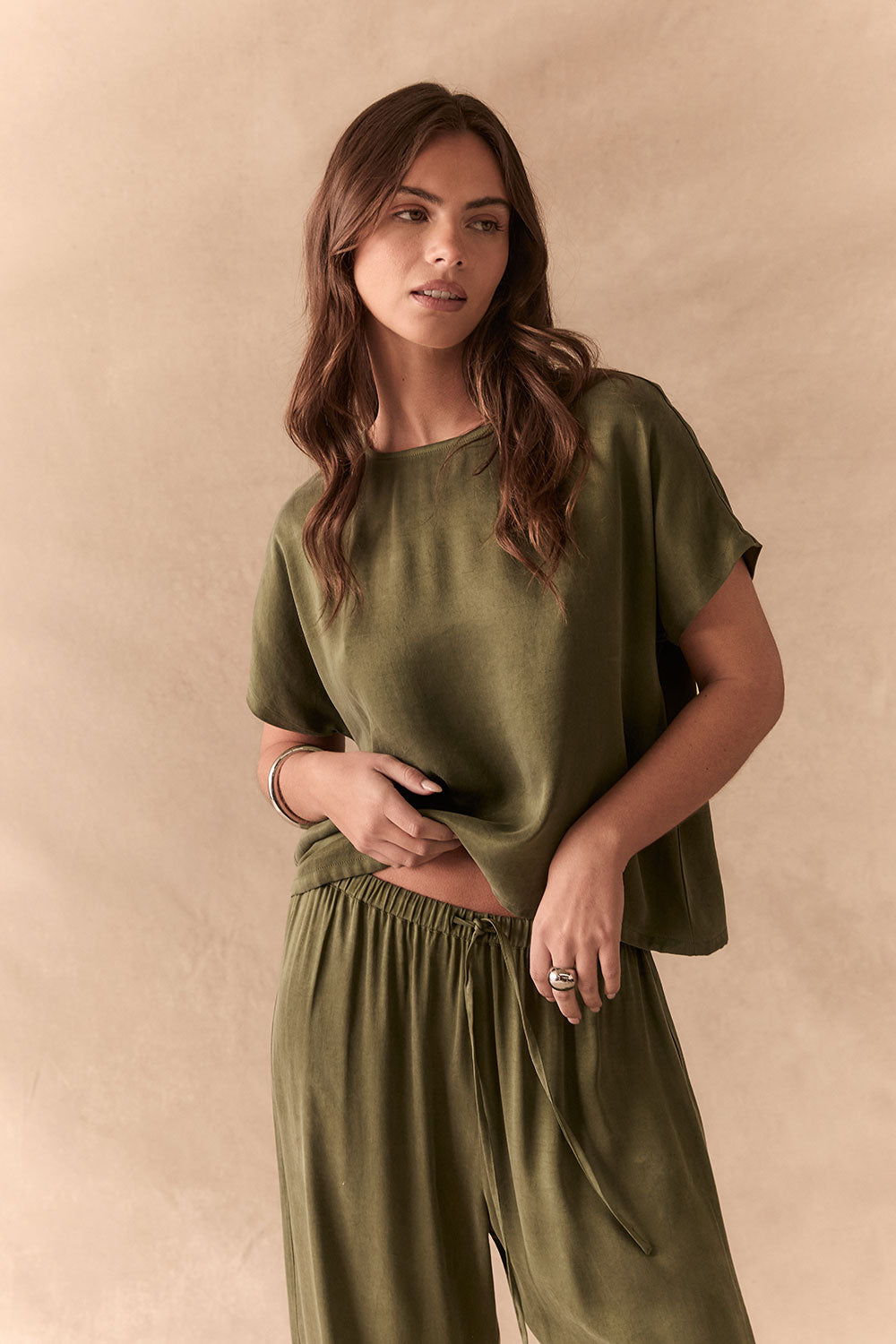 Woman wearing the Davis tee in bronze green against a beige background with matching Lee Pants