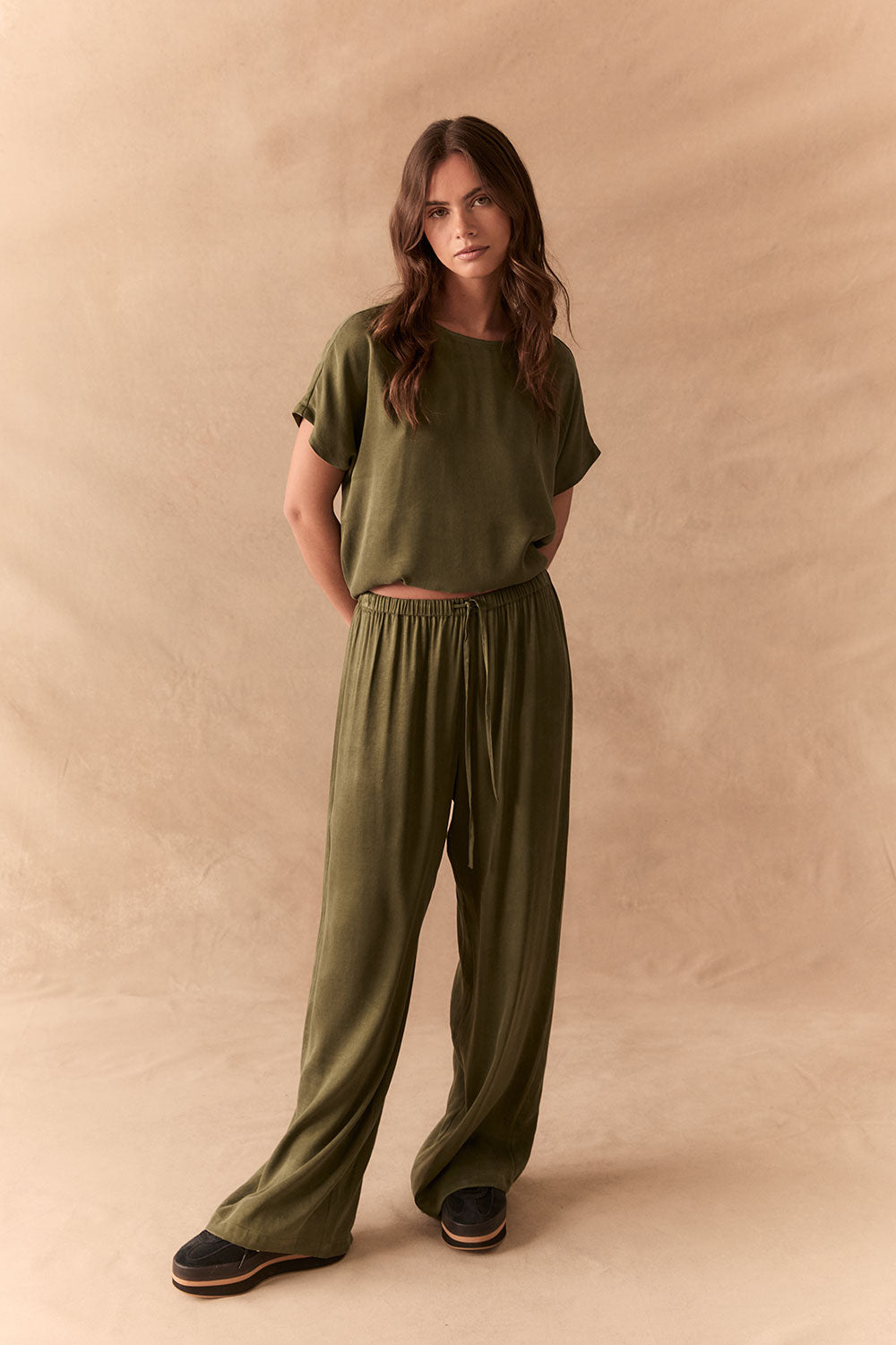 Full front view of Lee Trouser in bronze green with wide-leg silhouette and relaxed drape with matching tee against a beige background