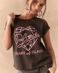 Woman wearing a black t-shirt with pink 'Blondie Heart of Glass' design on a beige background