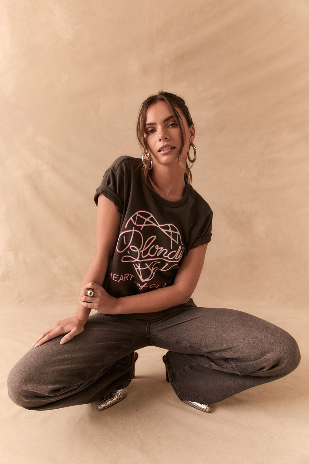 Woman wearing Blondie Heart of Glass tee in black, crouched on a beige background
