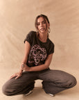 Woman wearing Blondie Heart of Glass tee in black, crouched on a beige background