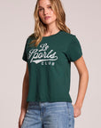 Side angle view of a woman wearing the Chaser Le Sports Club Tee on a neutral background with one hand on her hip