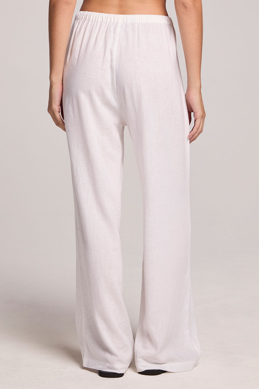 Back view of a woman wearing the Chaser Lee White Trouser  and black flip flops on a neutral background
