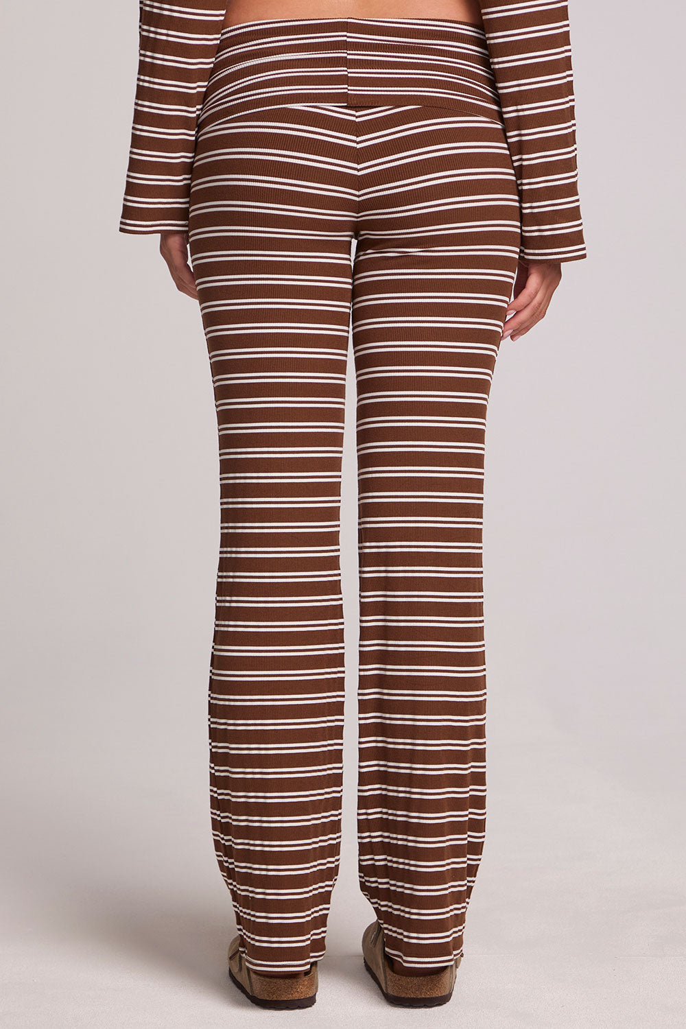 Back view of a woman wearing the Chaser Noorh Nutty Brown Stripe Pants on a neutral background with arms down at sides