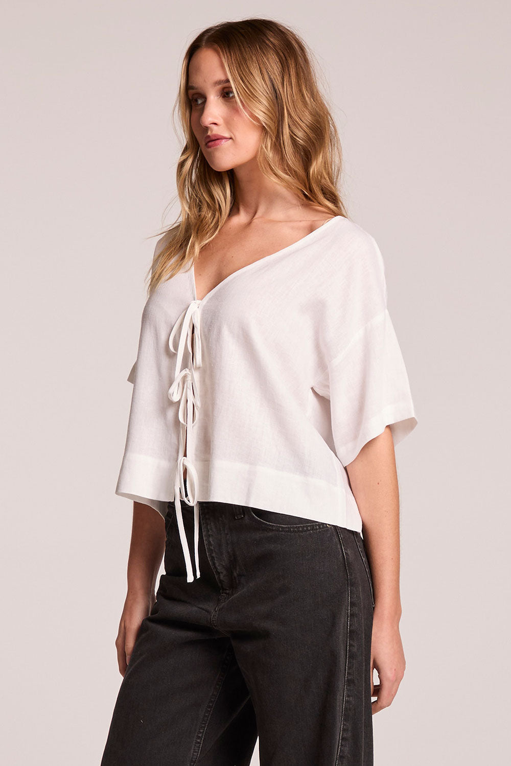 Side angle view of a woman wearing the Chaser Roselie White Blouse and black pants on a neutral background