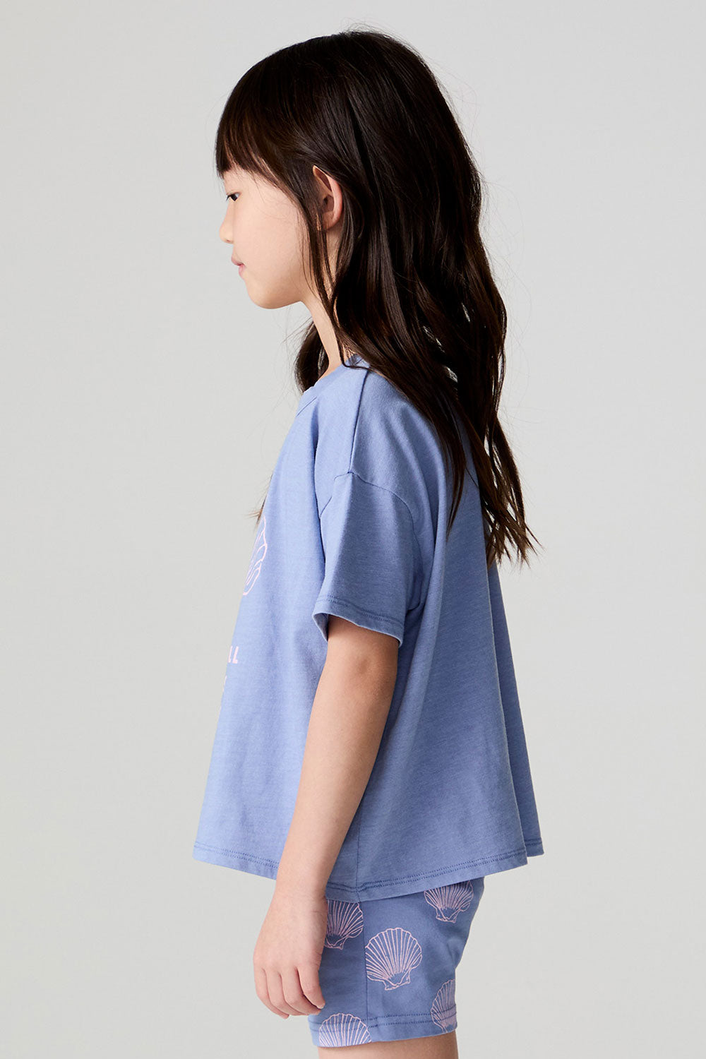 Side view of a girl wearing the Chaser Seashell Dreams Tee on a neutral background
