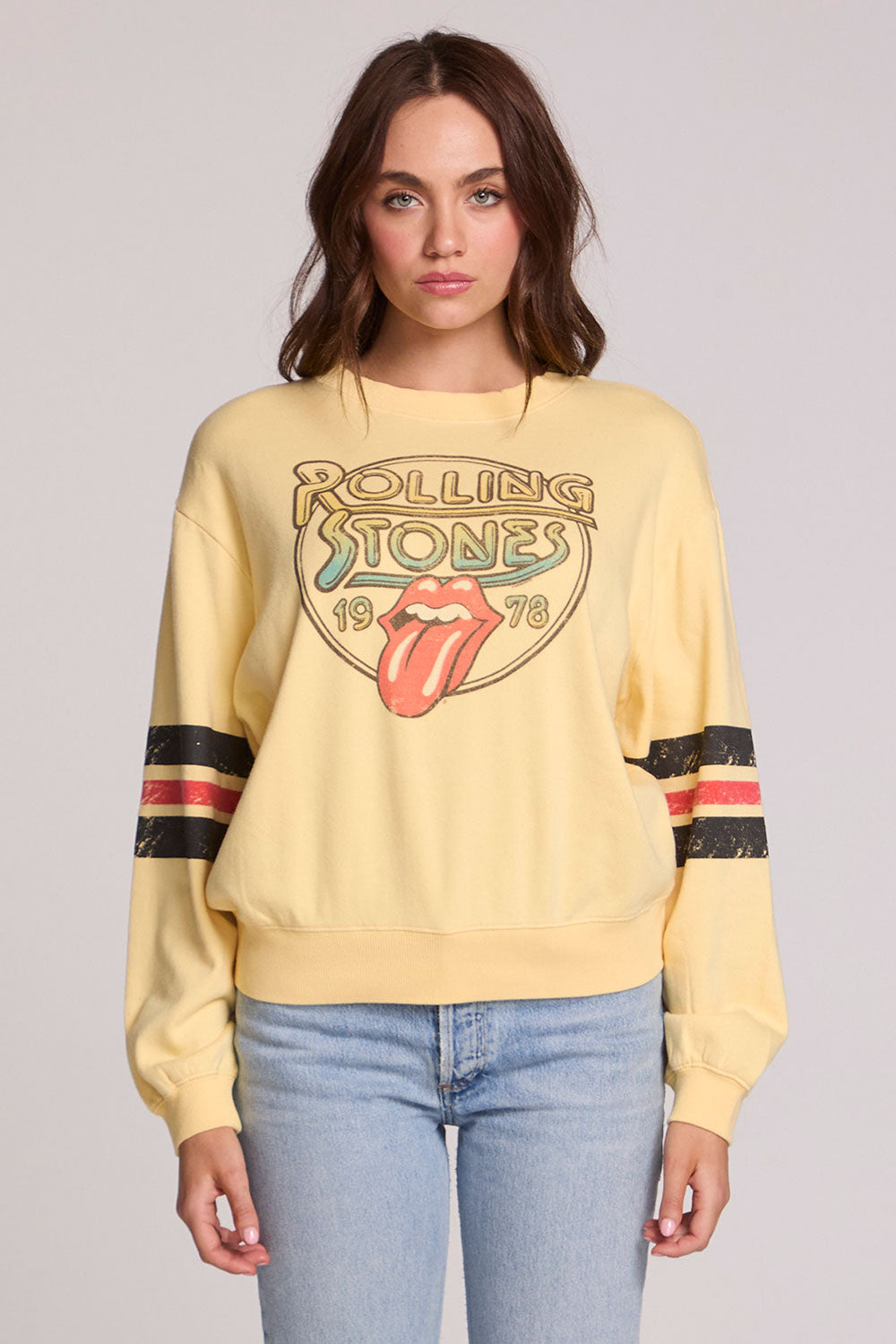 Front view of a woman wearing the Chaser  The Rolling Stones 1978 Long Sleeve Tee and jeans on a neutral background with arms lowered
