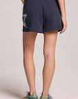 Side angle view of a woman wearing the Chaser Tie Dye Star Shorts  and shoes on a neutral background