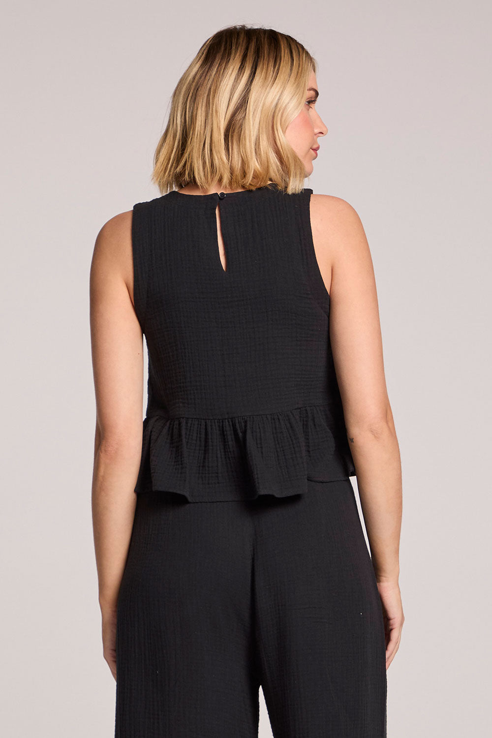 Back view of a woman wearing a black Chaser Liberty tank set on a neutral background