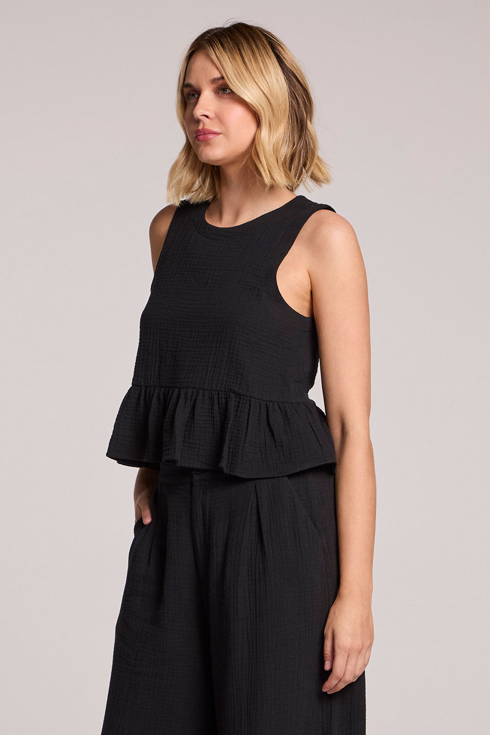 Side angle view of a blonde woman wearing a black Chaser Liberty tank set on a neutral background