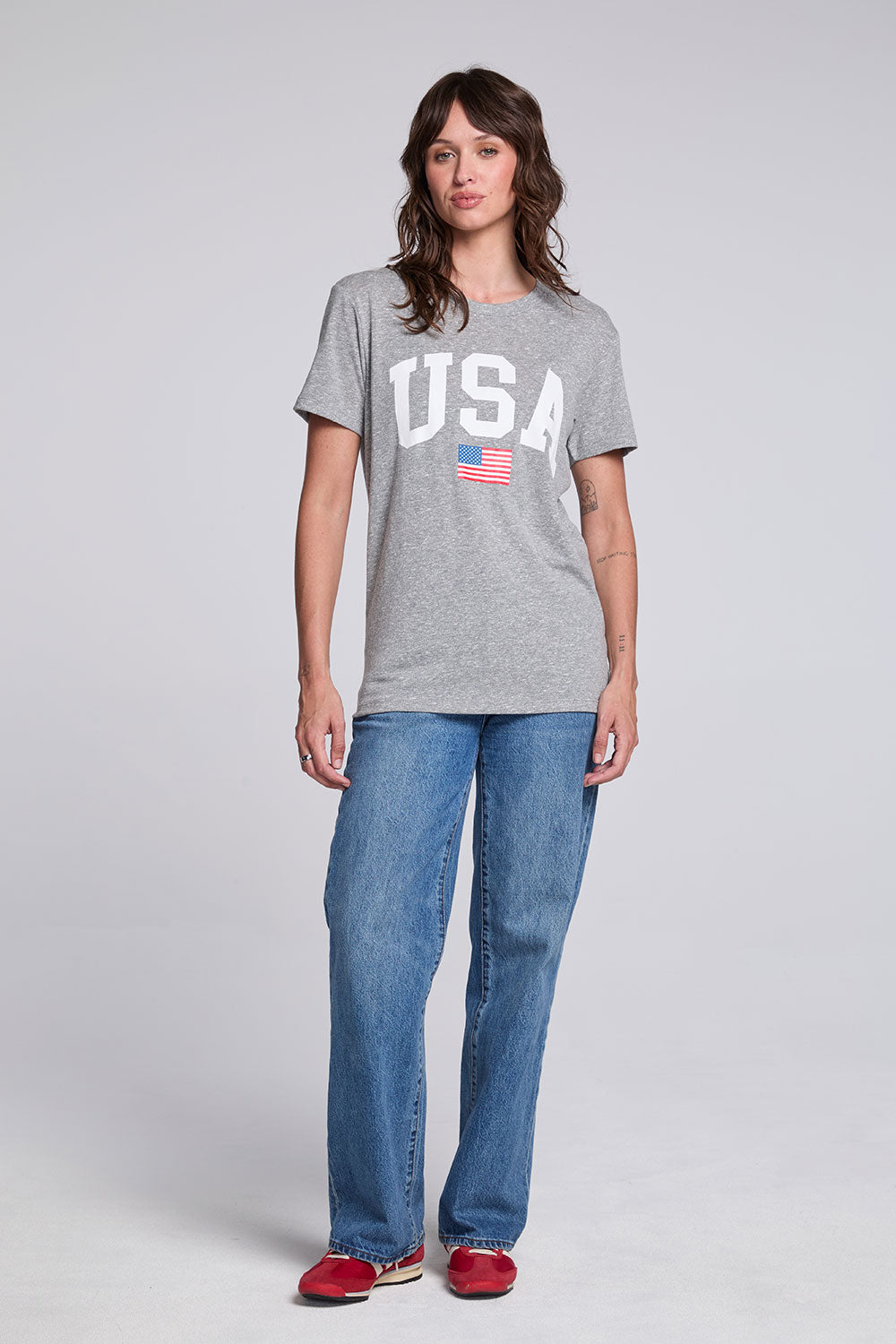 Model wearing Chaser USA Flag Oversized Tee in Streaky Grey styled with loose straight leg jeans and red sneakers
