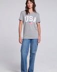 Model wearing Chaser USA Flag Oversized Tee in Streaky Grey styled with loose straight leg jeans and red sneakers