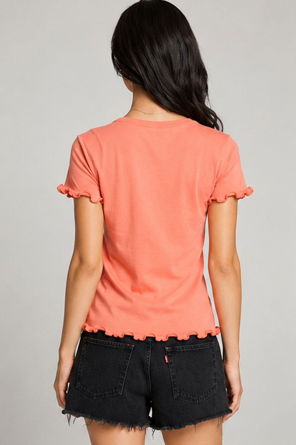 Back view of women’s coral Grateful Dead graphic tee with lettuce-edge ruffle sleeves and hem, styled with black denim shorts