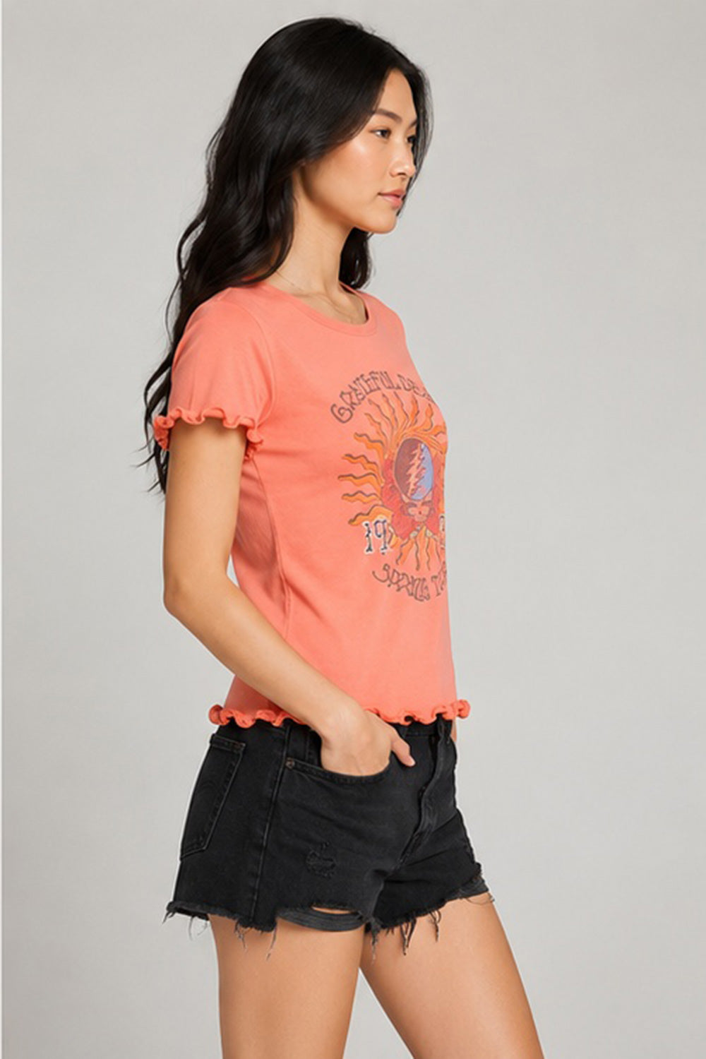 Side profile of women’s coral Grateful Dead 1977 Spring Tour graphic tee highlighting lettuce-edge ruffle sleeve detail and fitted silhouette
