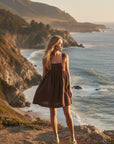 A blonde model on a Big Sur cliff at golden hour, the Kahlua linen mini catching the breeze with the Pacific stretching out behind her