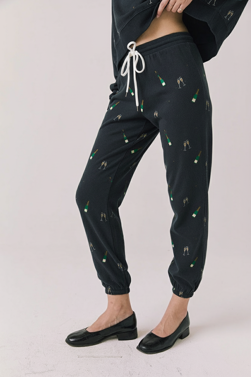 Side view of woman wearing Chaser’s black Champagne Party Joggers with white drawstrings on a light grey background